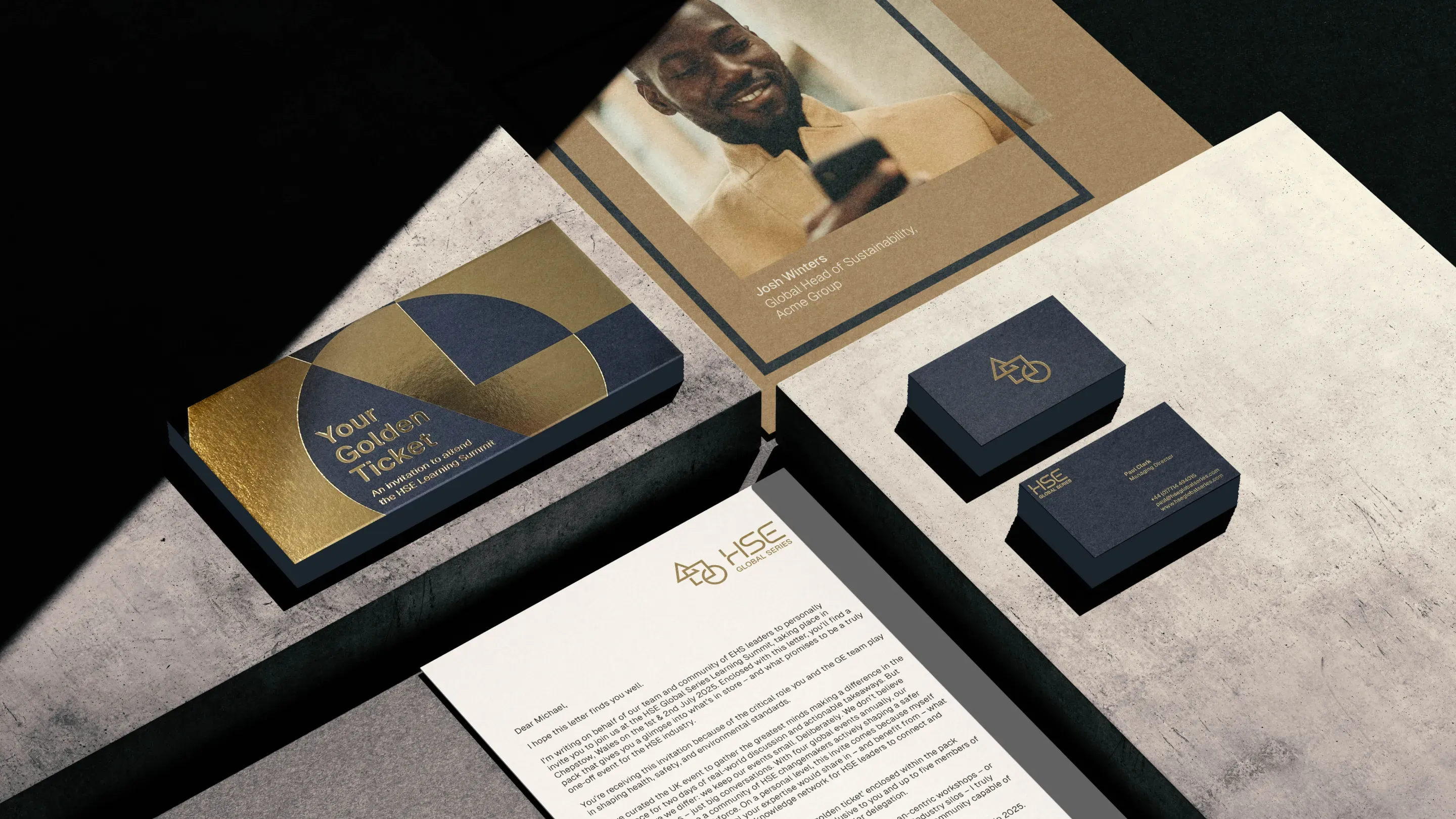 A flat lay of branded collateral, including a letter, two business cards, a gold and navy gift box labeled Your Golden Ticket, Global Series-themed stationery, and a photograph of a smiling man holding a phone